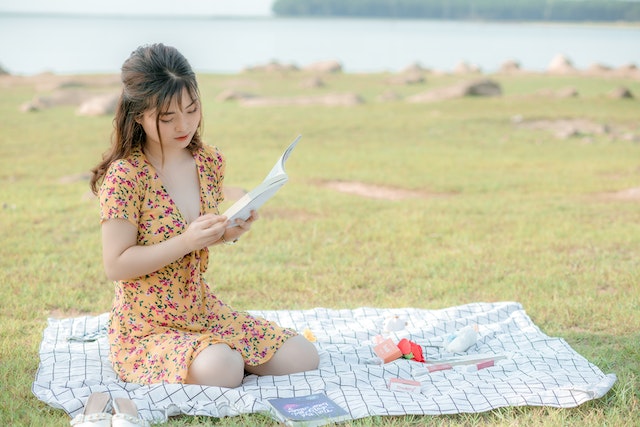 בחורה יושבת על מחצלת על הדשא וקוראת ספר